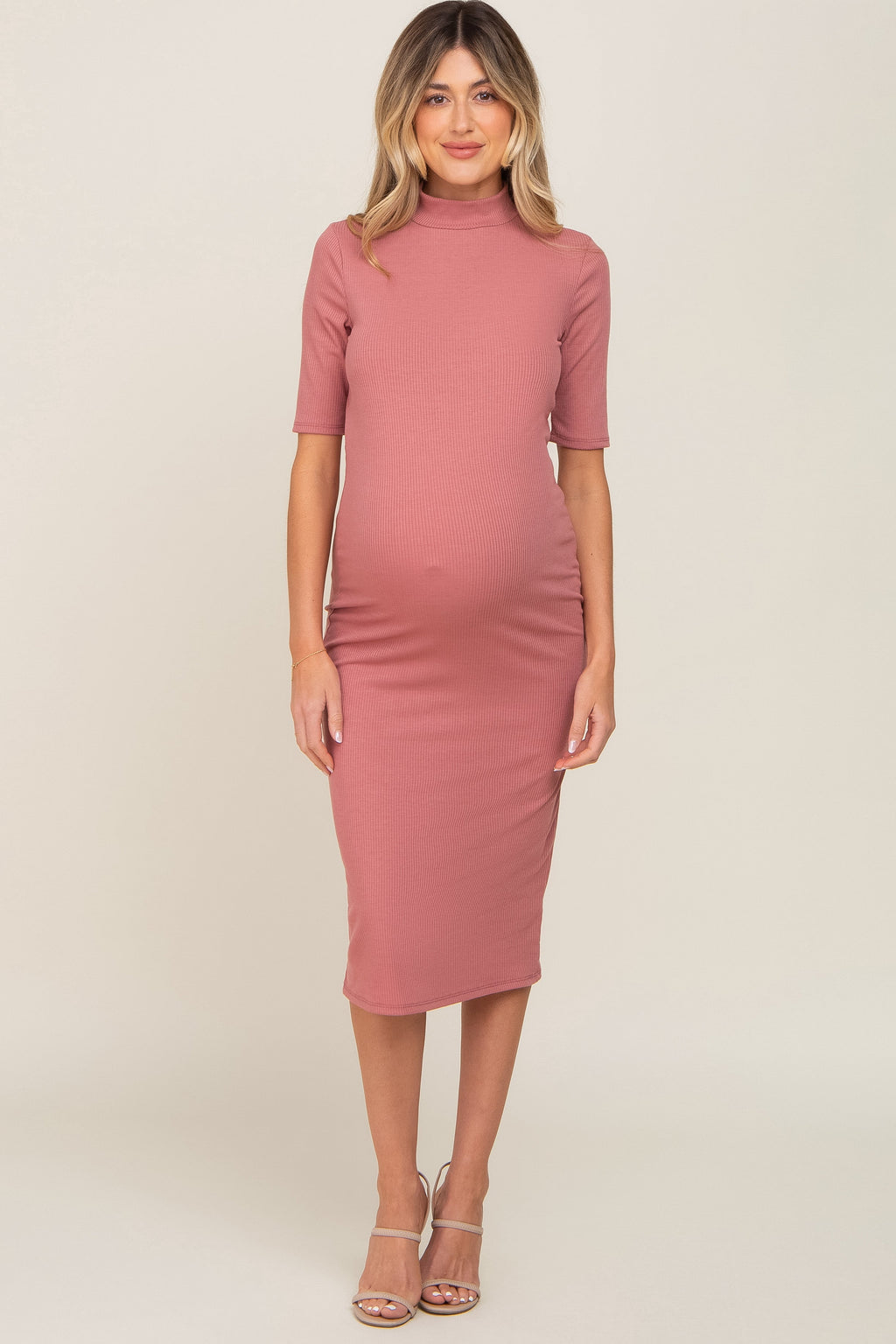 Pregnant woman wearing a soft mauve ribbed mock neck midi dress with long sleeves.