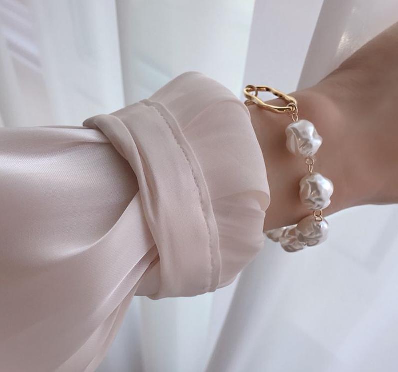 Four-row gold-tone link chain bracelet with imitation pearls on a neutral background