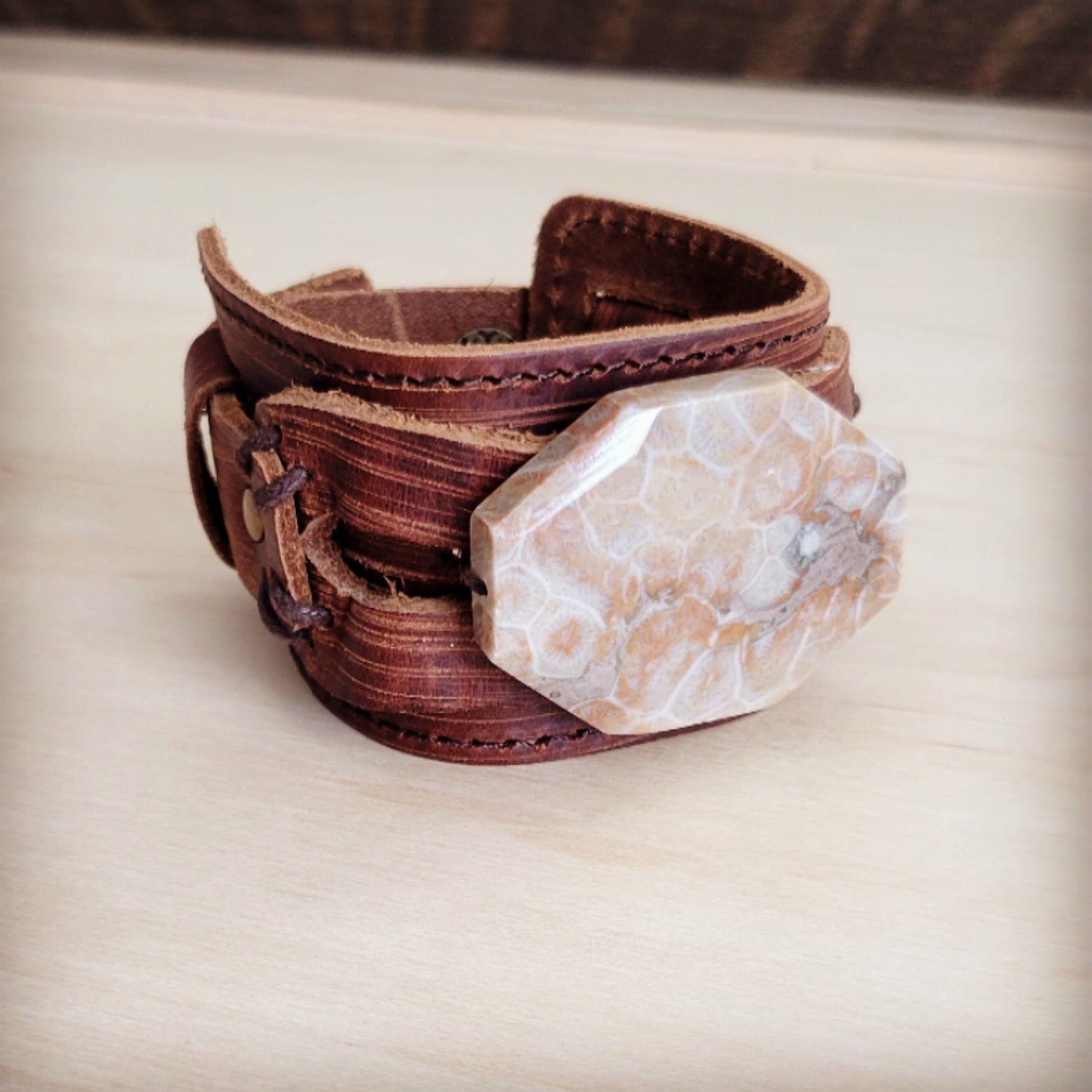 Close up of a brown distressed leather cuff bracelet featuring a large octagonal fossil corral stone center piece.