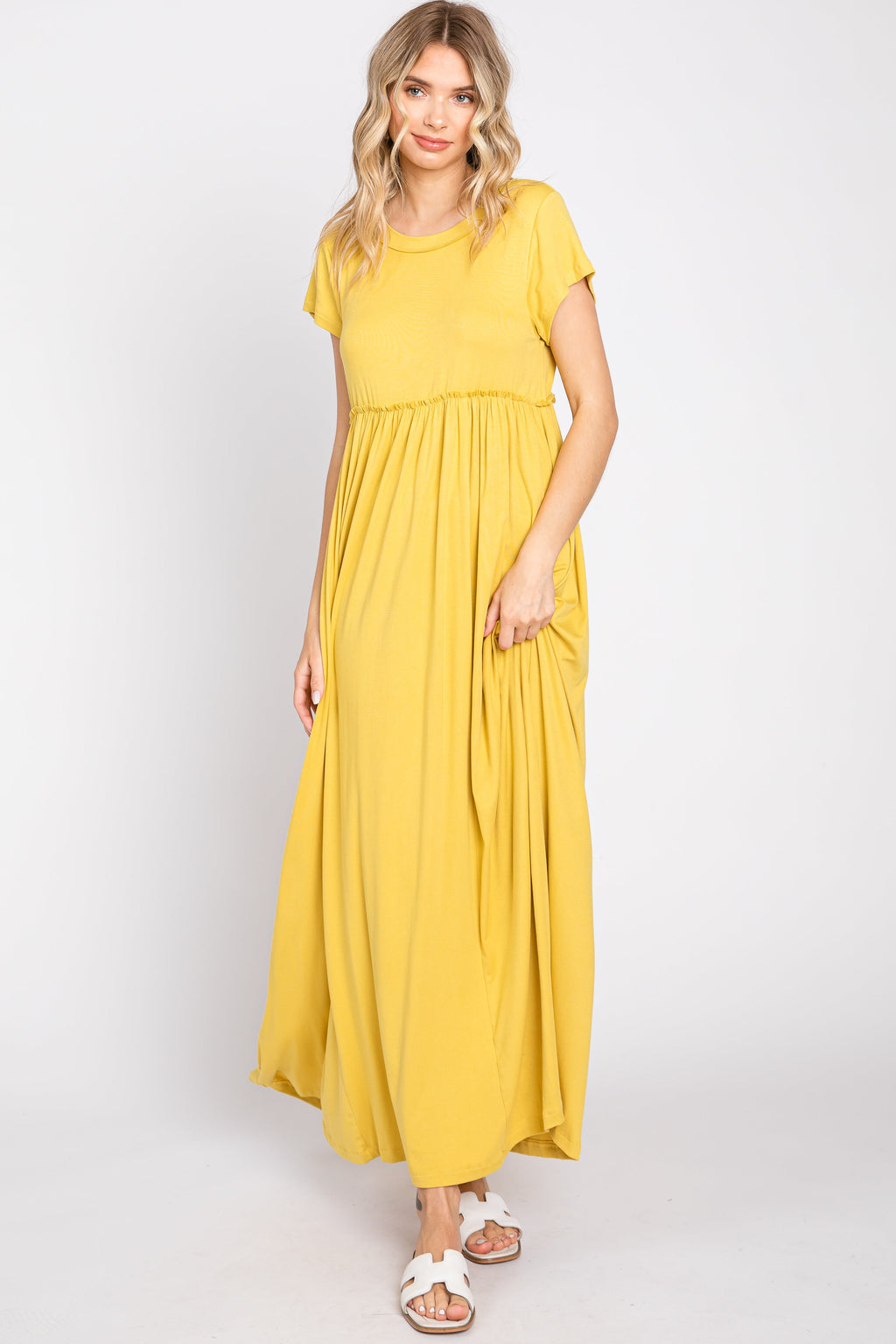 A woman wearing a solid yellow short sleeve maxi dress with a ruffled waist and side pockets against a plain backdrop.