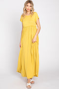 A woman wearing a solid yellow short sleeve maxi dress with a ruffled waist and side pockets against a plain backdrop.