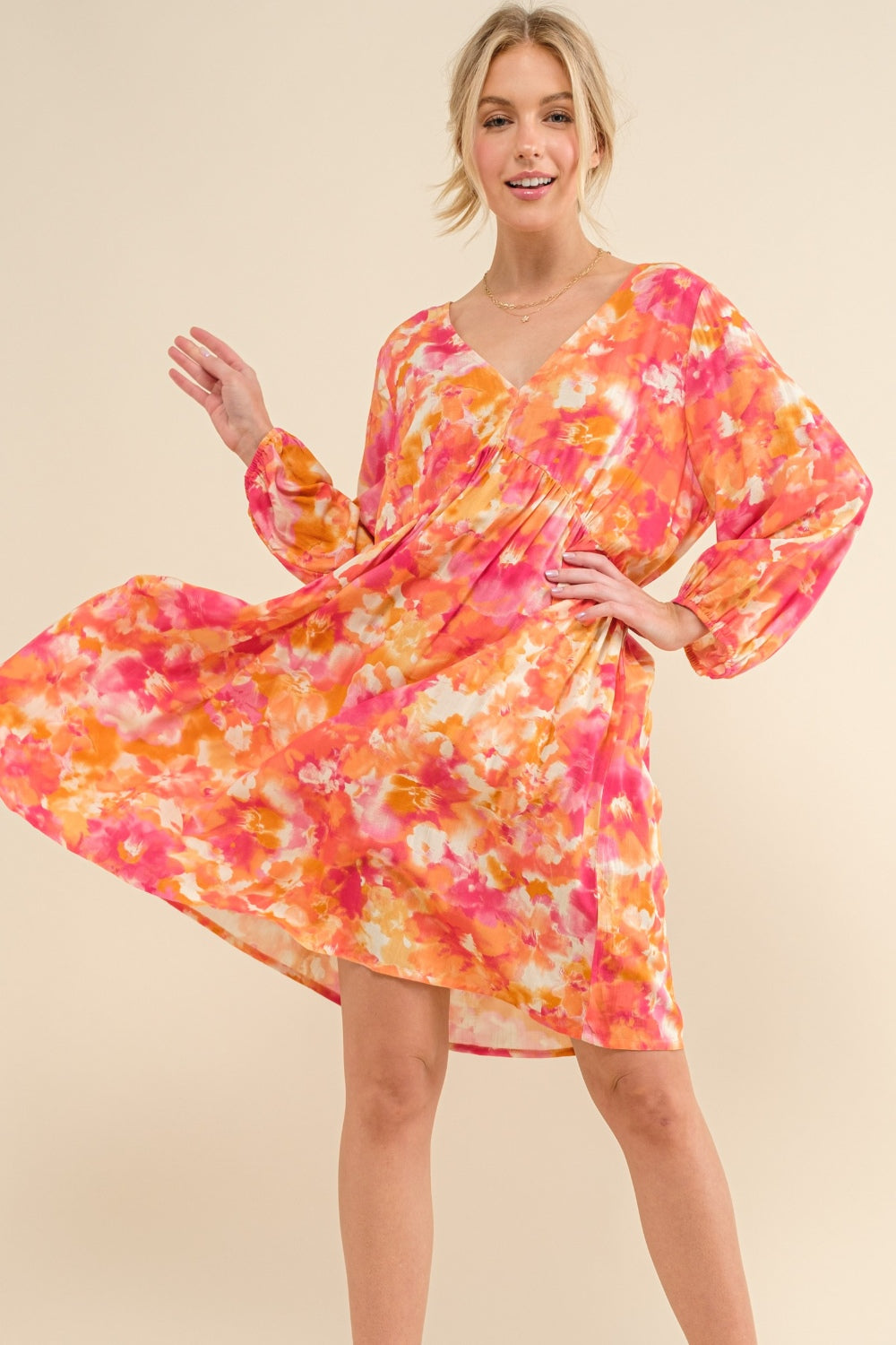 Woman wearing a romantic pink and orange floral long sleeve summer dress with a tie-back detail.