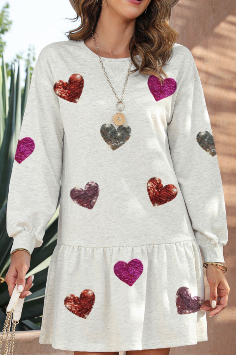 Girl wearing a long sleeve knit mini dress with sequin heart detail in light grey