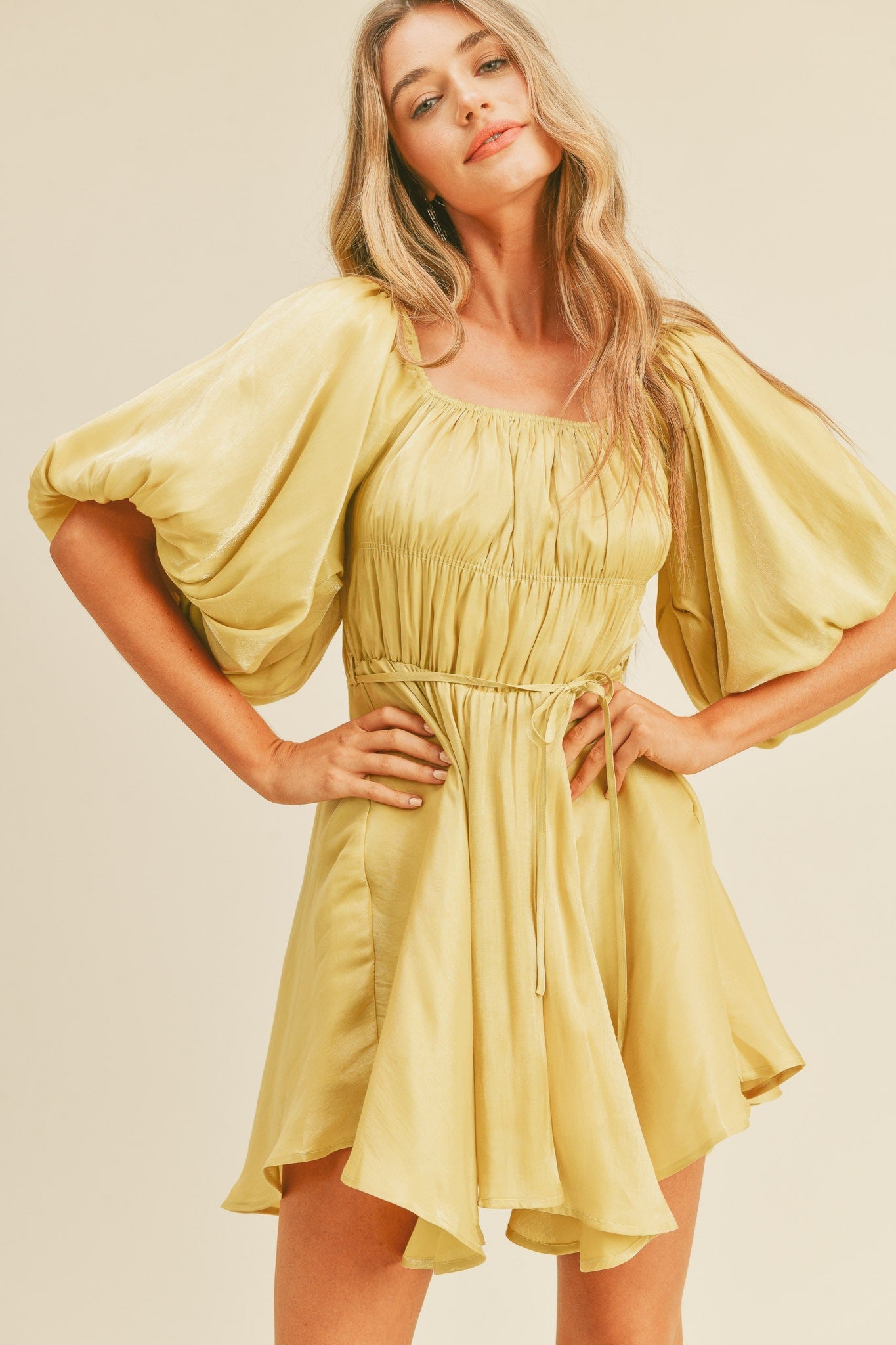 A woman wearing a yellow metallic mini dress with bubble sleeves and a flared skirt.
