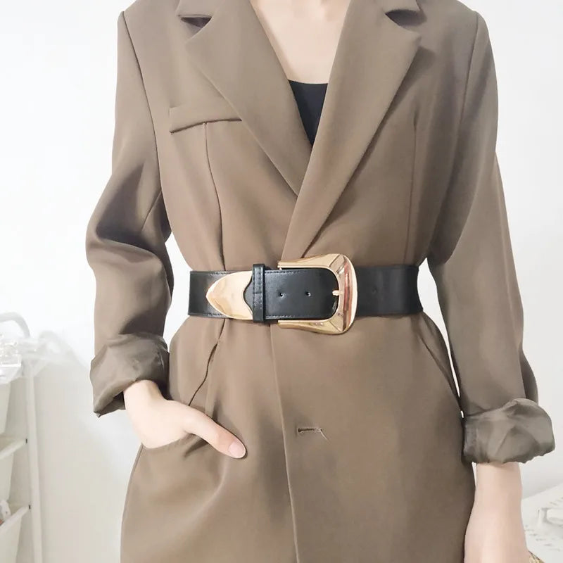 Woman wearing a Harajuku style black wide elastic waist belt with a large gold buckle over a brown blazer, showcasing a stylish cinched waist.