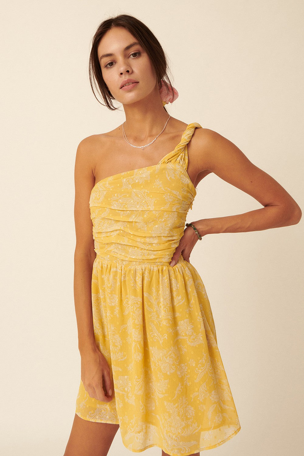 Model wearing a bright yellow floral swiss dot chiffon one shoulder mini dress with ruched bodice detail
