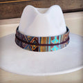 Close up of a 1.5 inch wide genuine leather hat band with a blue and brown Navajo print, wrapped around a white hat.