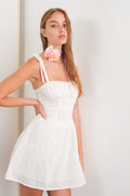 A model wearing a white mini dress with a corset bodice and tie-shoulder straps against a plain background