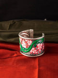 Hand-painted brass kada bracelet with vibrant red and green floral designs on an oxidized silver-plated wide cuff
