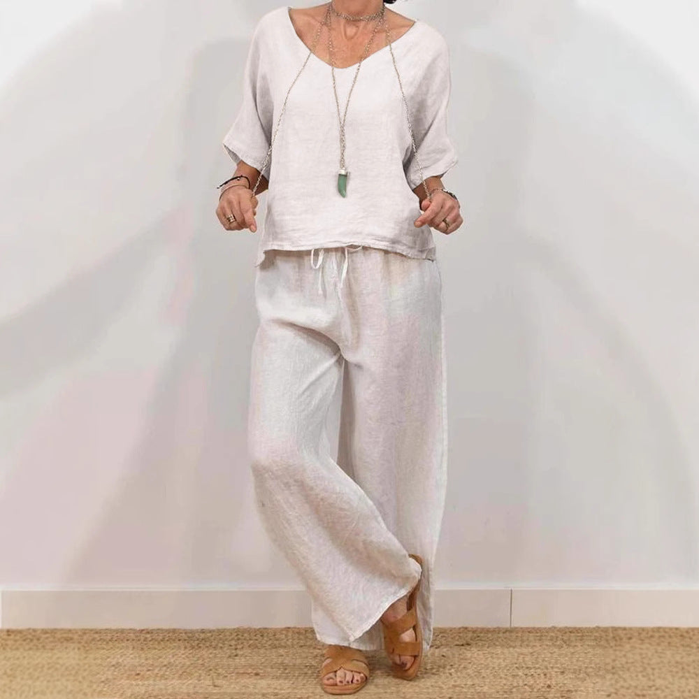 A model wearing a relaxed-fit V-neck pullover top and matching wide-leg pants in a light grey color, featuring three-quarter sleeves and a drawstring waist.