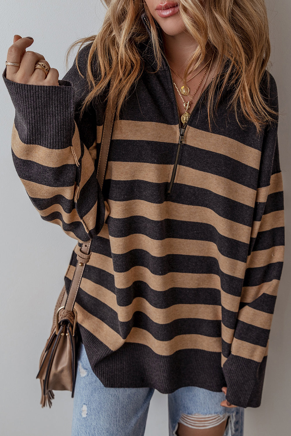 Person wearing a black and beige striped sweater with a plain background