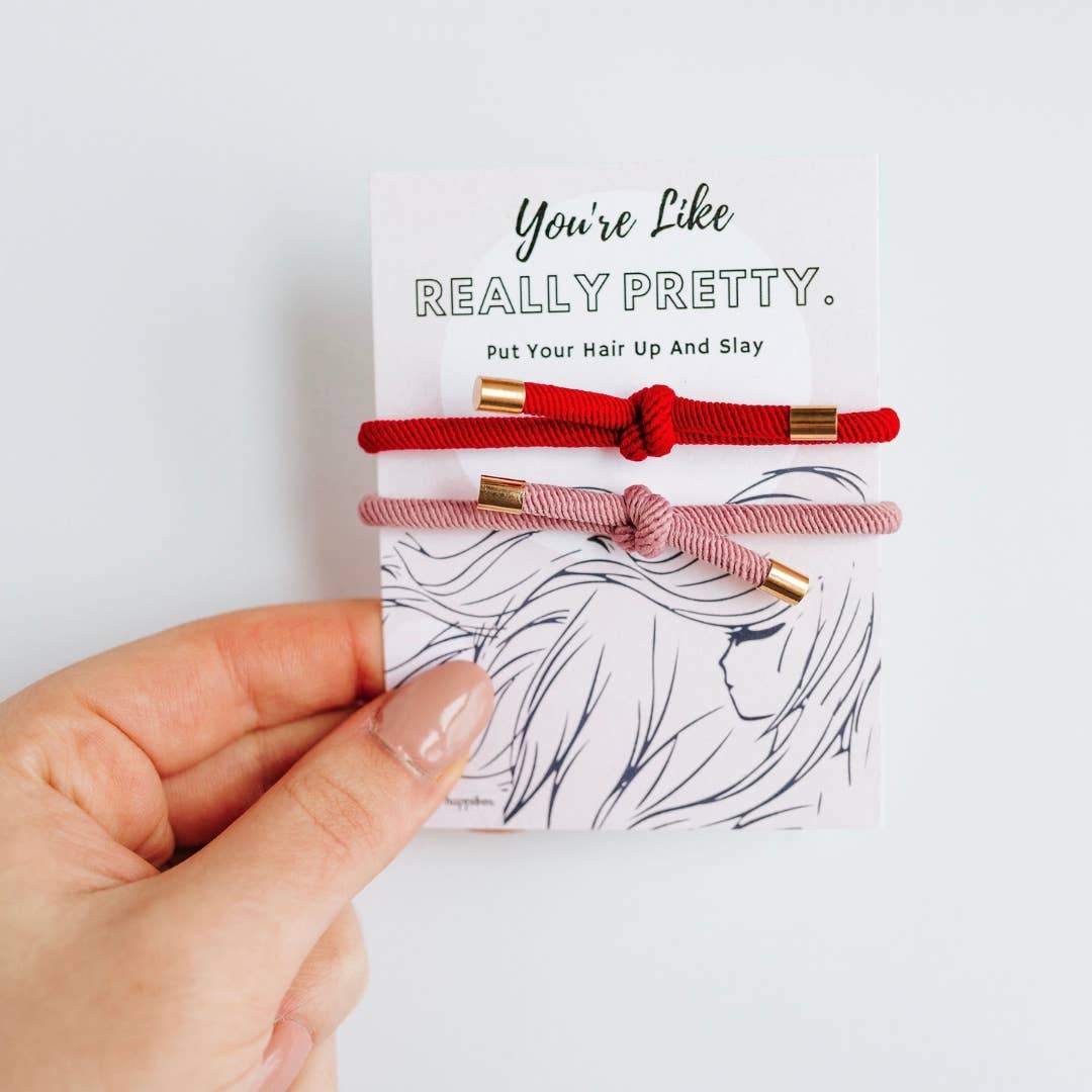 A hand holding a white card featuring a pair of colorful knotted elastic hair ties with the quote You're Like Really Pretty printed at the top.
