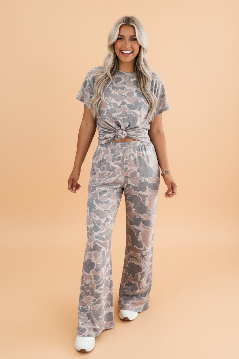 A woman wearing a matching camo print set with a short sleeve top and wide leg pants.