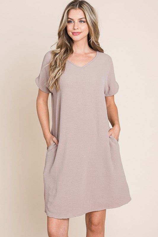 A minimalist taupe V-neck short sleeve dress with visible functional pockets.