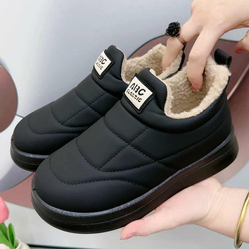 A pair of black quilted winter slip-on shoes with plush lining held in hand.