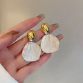 Close up of two-tone irregular shell texture statement earrings in gold and silver finish