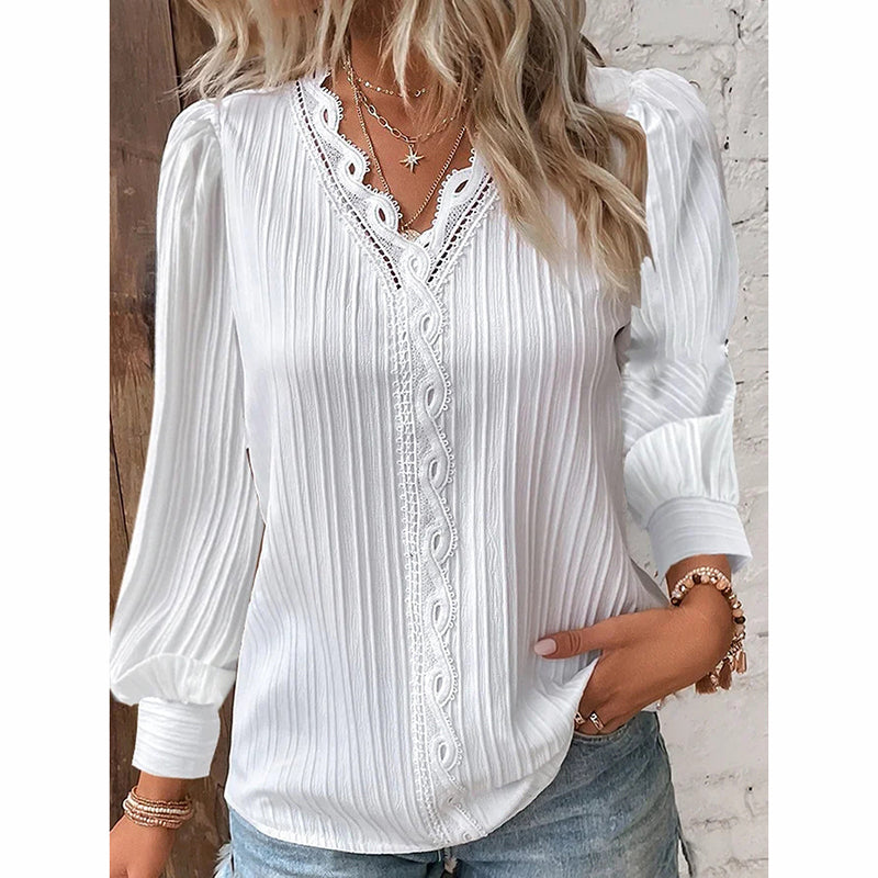 A woman wearing a white, long-sleeve blouse with intricate lace trim along the v-neckline and subtle vertical texture.