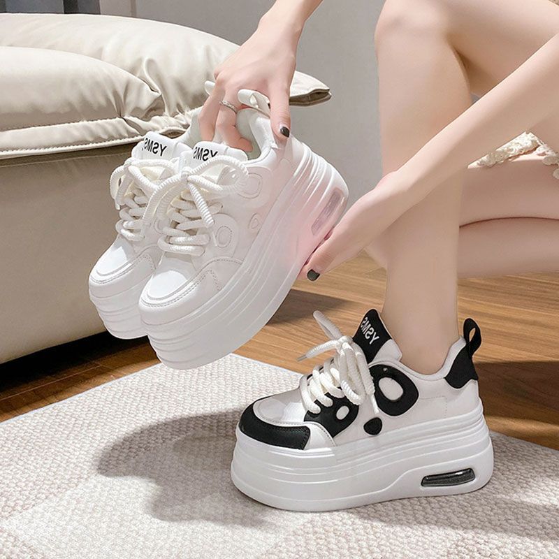 A pair of white and black thick-soled platform sneakers with a panda-inspired aesthetic held by a person.