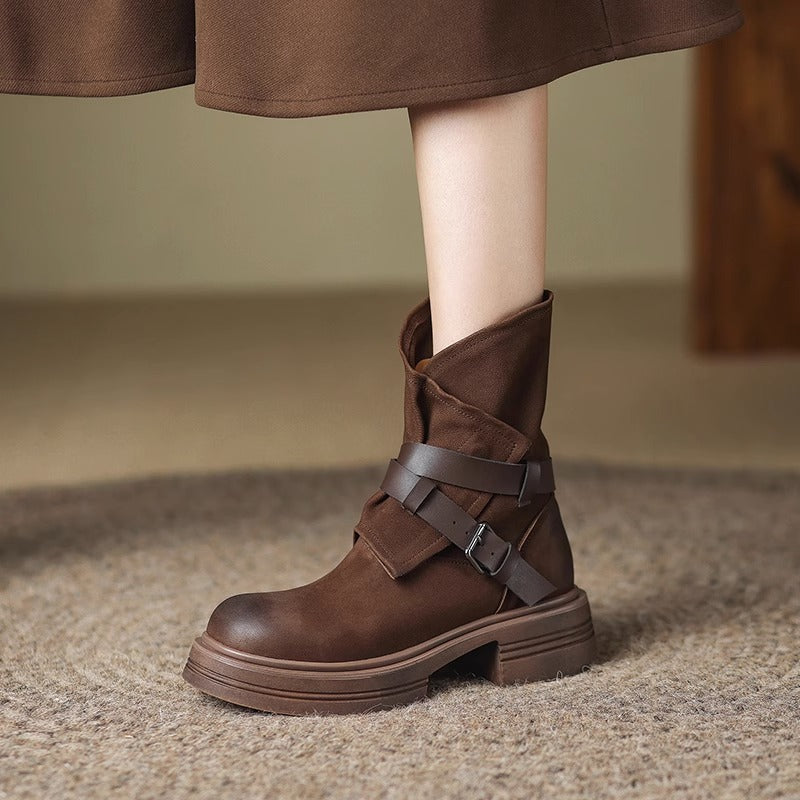 A woman wearing brown retro British-style ankle boots with a buckled strap detail on a textured rug