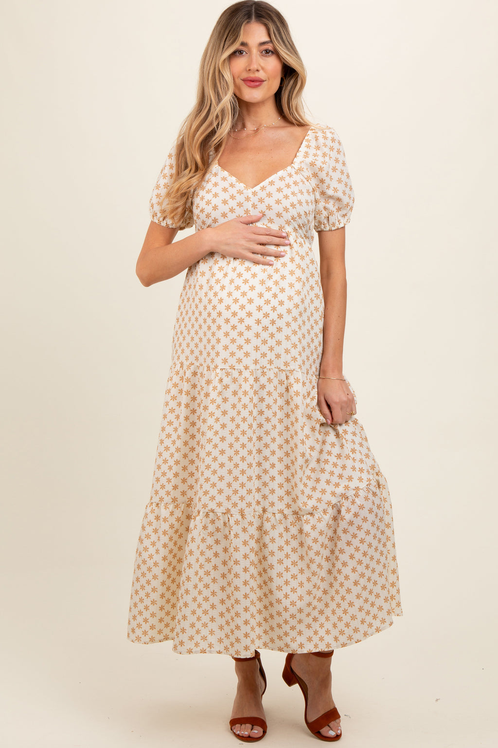 Woman wearing a yellow floral print maternity maxi dress with puff sleeves and a tiered skirt.