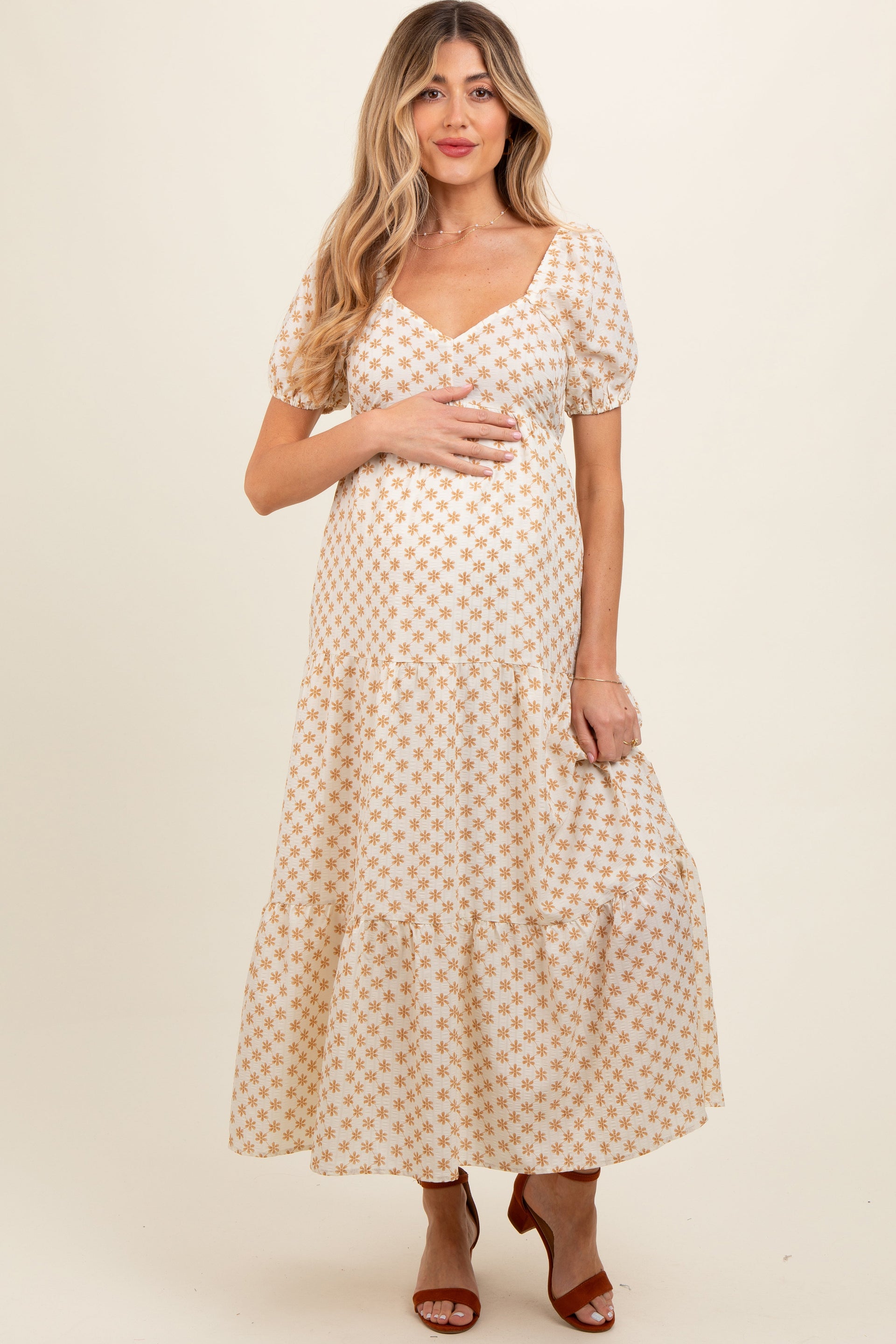 Woman wearing a yellow floral print maternity maxi dress with puff sleeves and a tiered skirt.