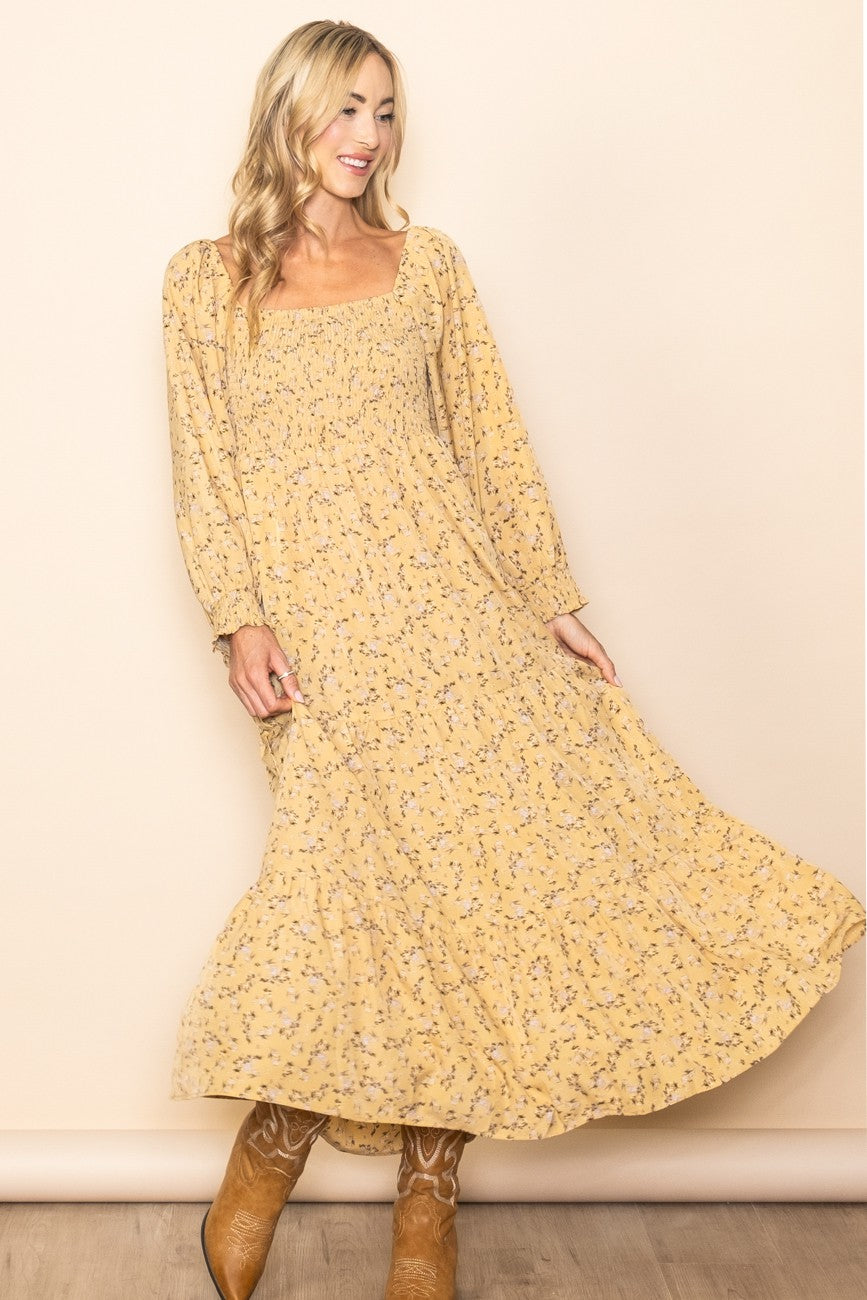 A woman wearing a Yellow Floral Smocked Long Sleeve Maxi Dress with a fitted bodice and flowing skirt.