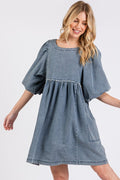 Woman wearing a vintage-inspired washed denim dress with puff sleeves and round neckline