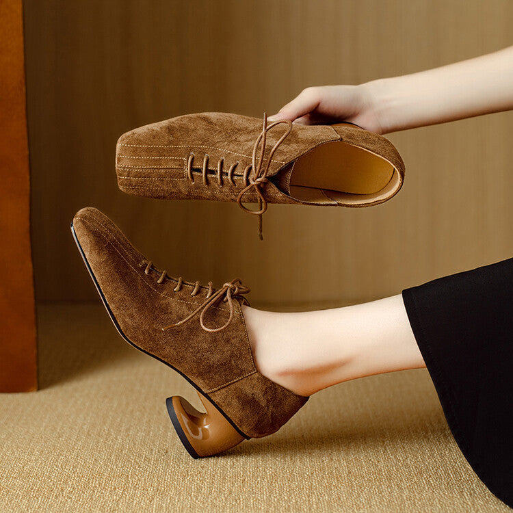 Close up of a woman wearing brown suede square toe pumps with a chunky heel and lace-up detail.