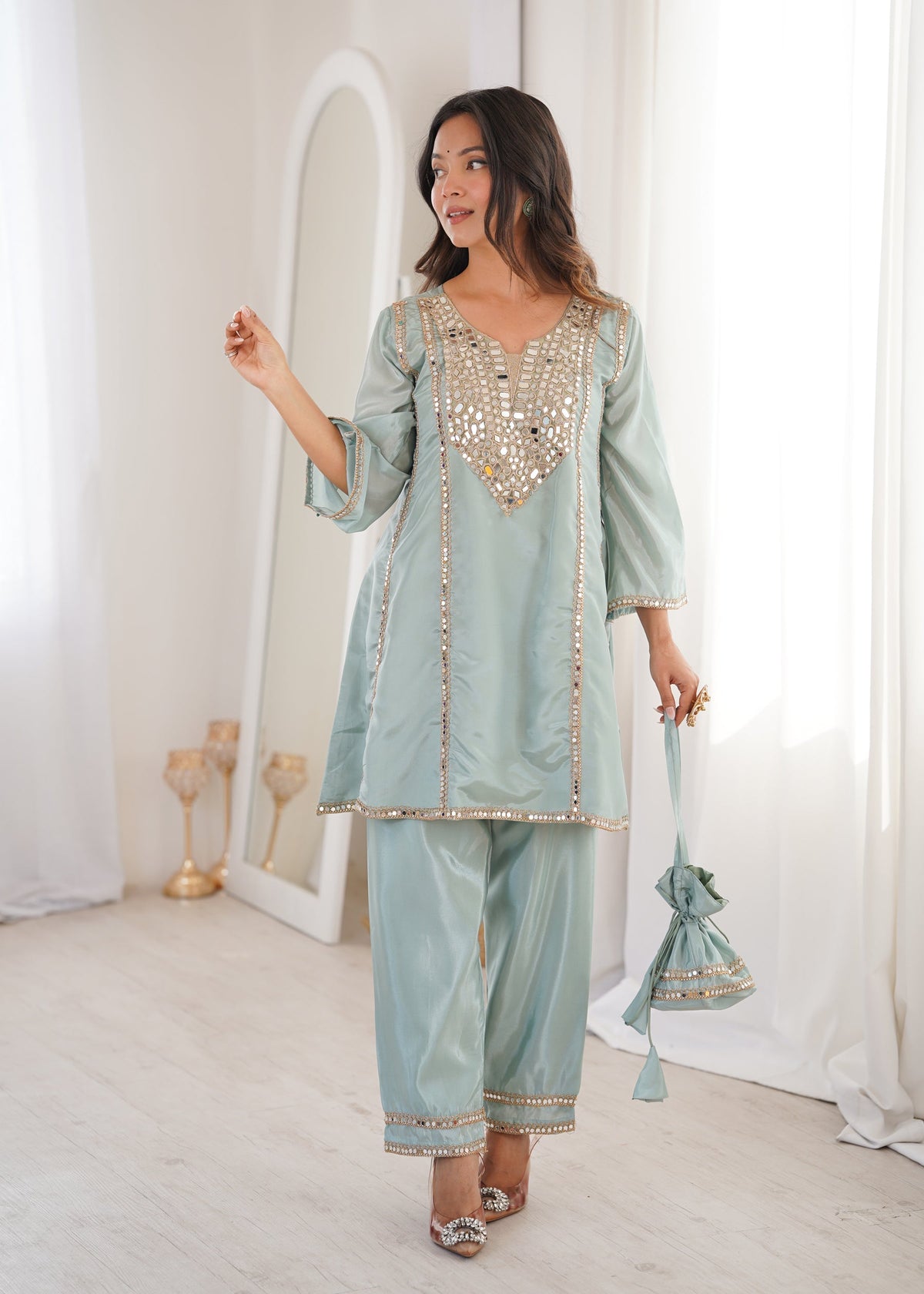 Woman wearing a sky-blue silk kurta set with real mirror embroidery and matching batwa bag