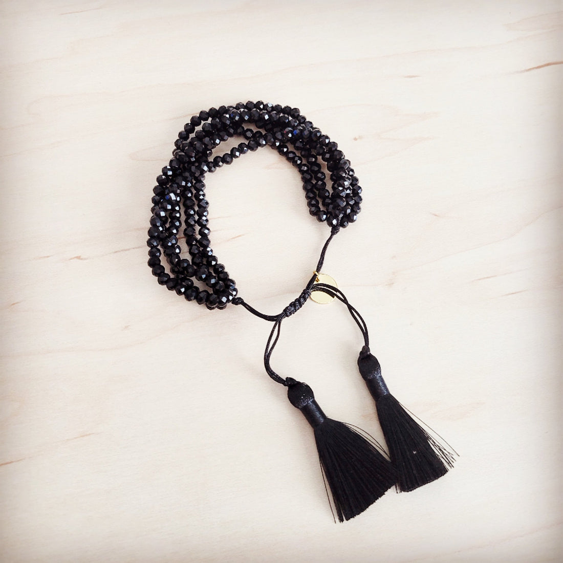 Close up of a multi-strand black faceted bead bracelet with black fabric tassels and an adjustable drawstring clasp worn on a wrist.