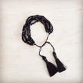 Close up of a multi-strand black faceted bead bracelet with black fabric tassels and an adjustable drawstring clasp worn on a wrist.