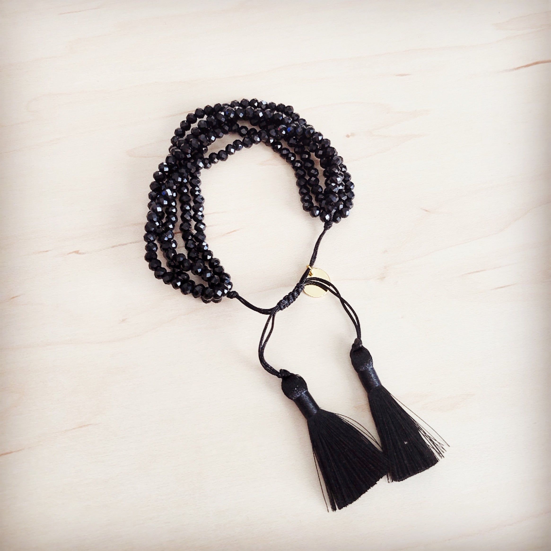 Close up of a multi-strand black faceted bead bracelet with black fabric tassels and an adjustable drawstring clasp worn on a wrist.