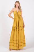 A woman wearing a vibrant yellow sleeveless maxi dress with a deep v-neck, halter straps, and tiered ruffle details against a white background.