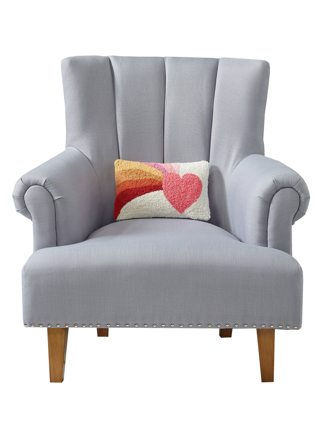 Small rectangular throw pillow with a vibrant, hooked wool design showing a heart and rainbow motif, resting on a gray upholstered chair.