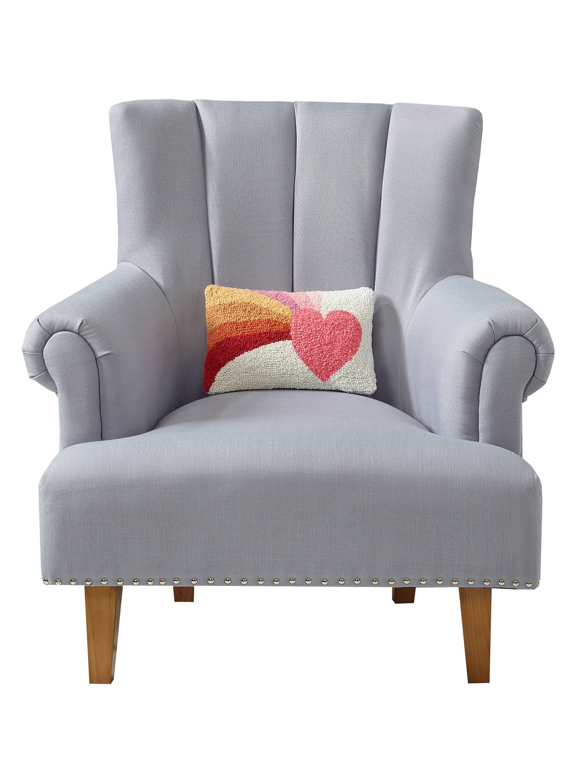 Small rectangular throw pillow with a vibrant, hooked wool design showing a heart and rainbow motif, resting on a gray upholstered chair.
