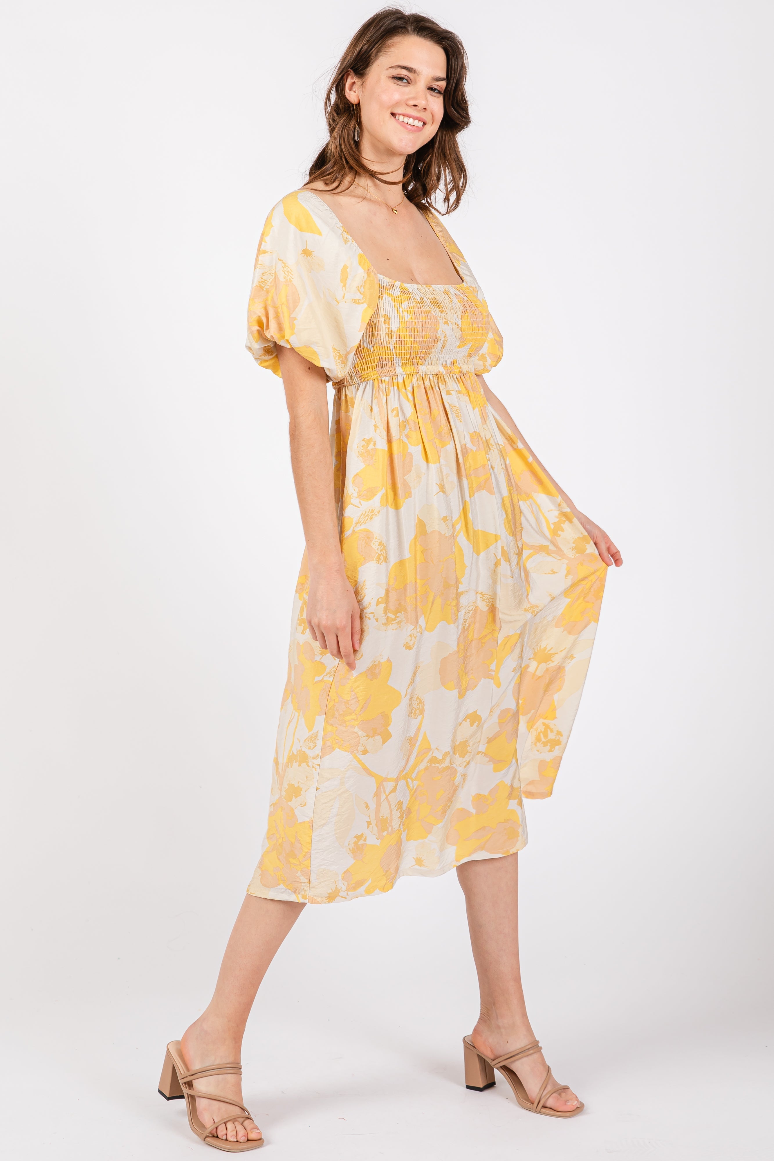 A woman wearing a yellow and white floral print midi dress with a square neckline, puff sleeves, and a smocked bodice against a white background.