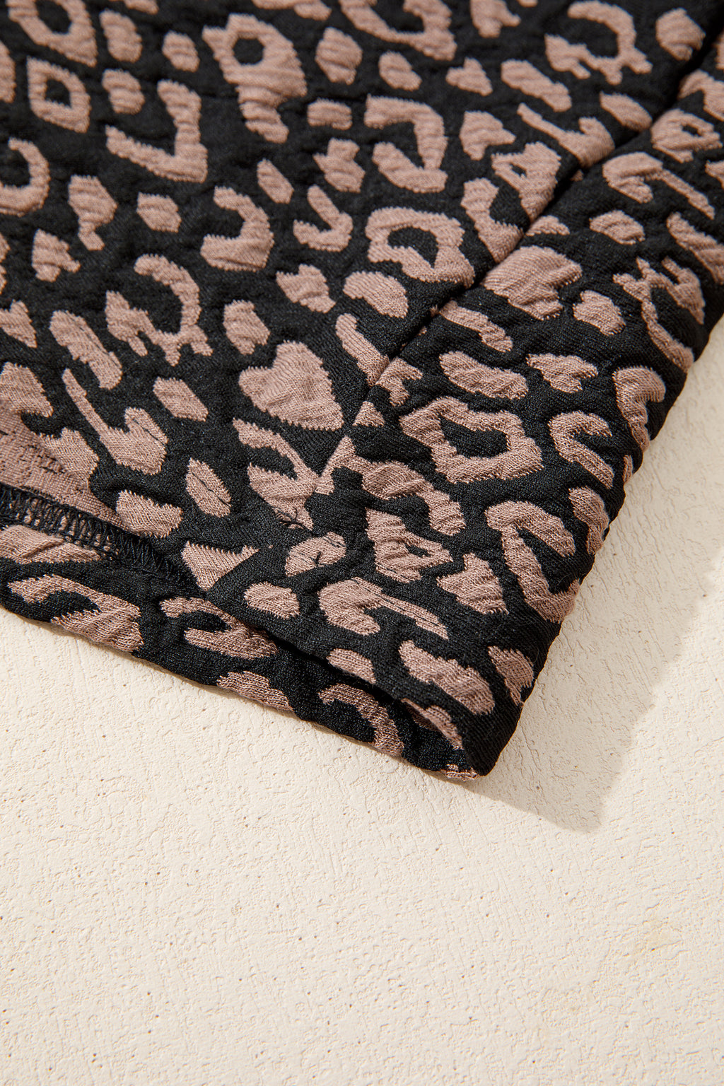 Close-up of black fabric with a pink leopard print pattern on a beige background