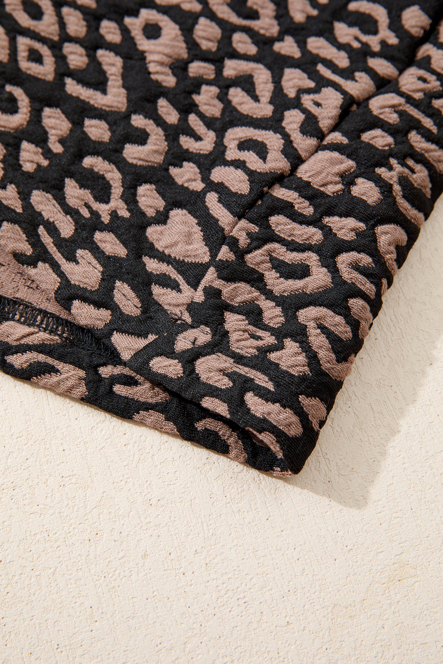 Close-up of black fabric with a pink leopard print pattern on a beige background