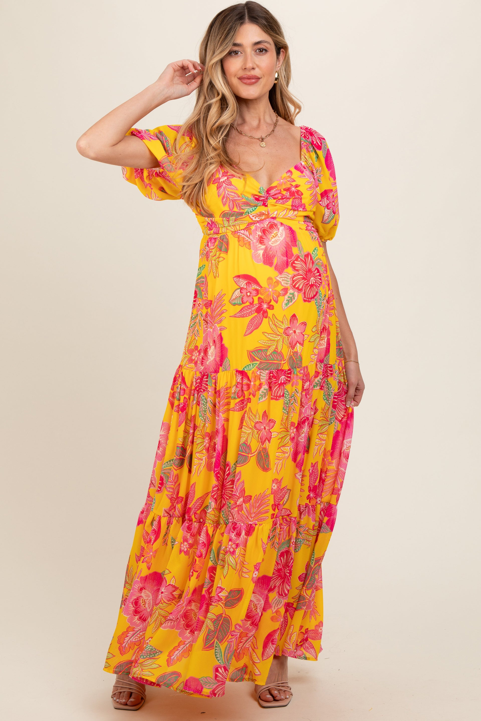 A pregnant woman wearing a bright yellow floral print maxi dress with a sweetheart neckline and tiered skirt.