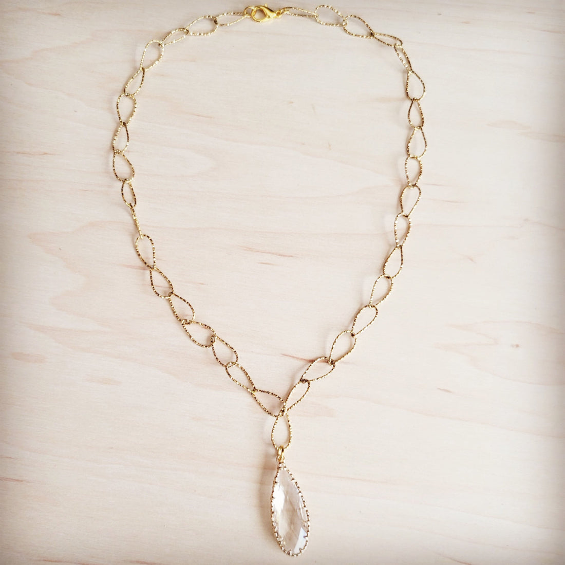 Gold-tone chain necklace with textured oval links and a single faceted clear teardrop pendant.