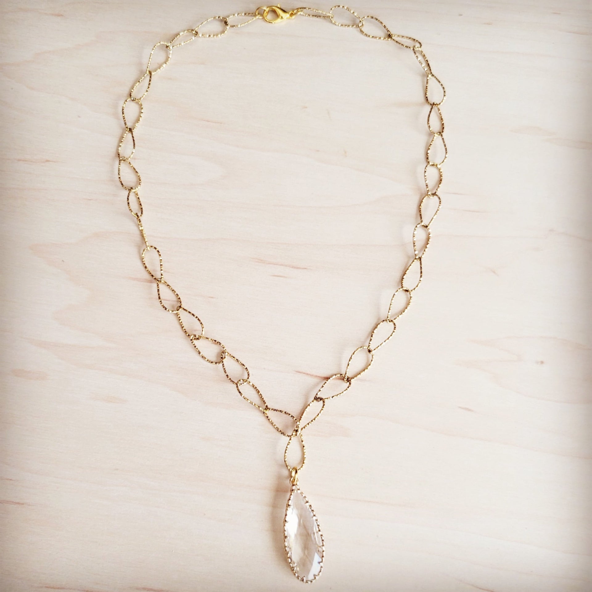 Gold-tone chain necklace with textured oval links and a single faceted clear teardrop pendant.
