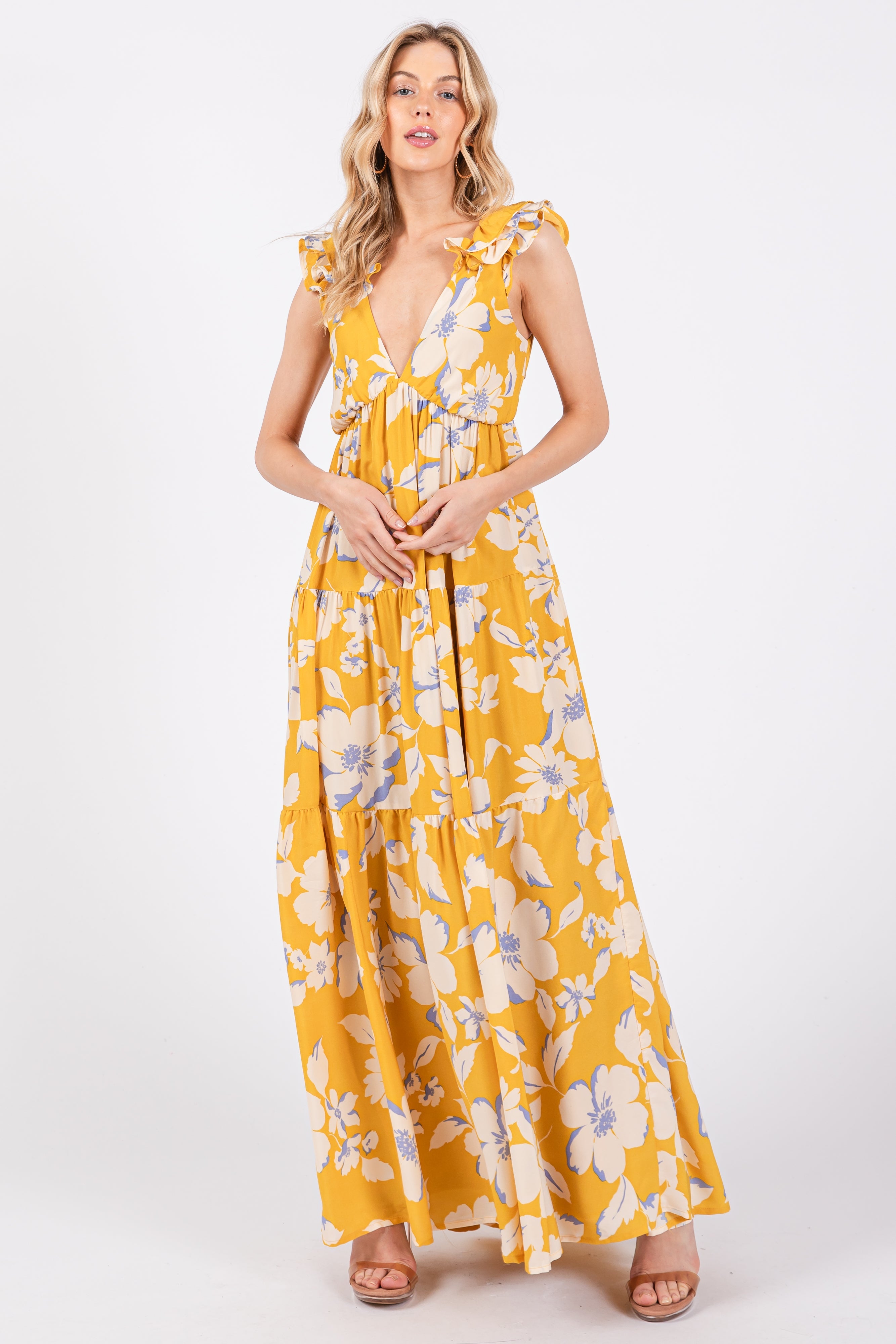 A woman wearing a vibrant yellow floral maxi dress with a deep V-neck, flutter sleeves, and an open back design, standing against a white studio background.