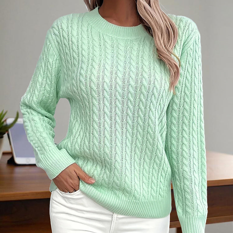 A woman wearing a textured crew-neck cable knit sweater in light green with long sleeves.