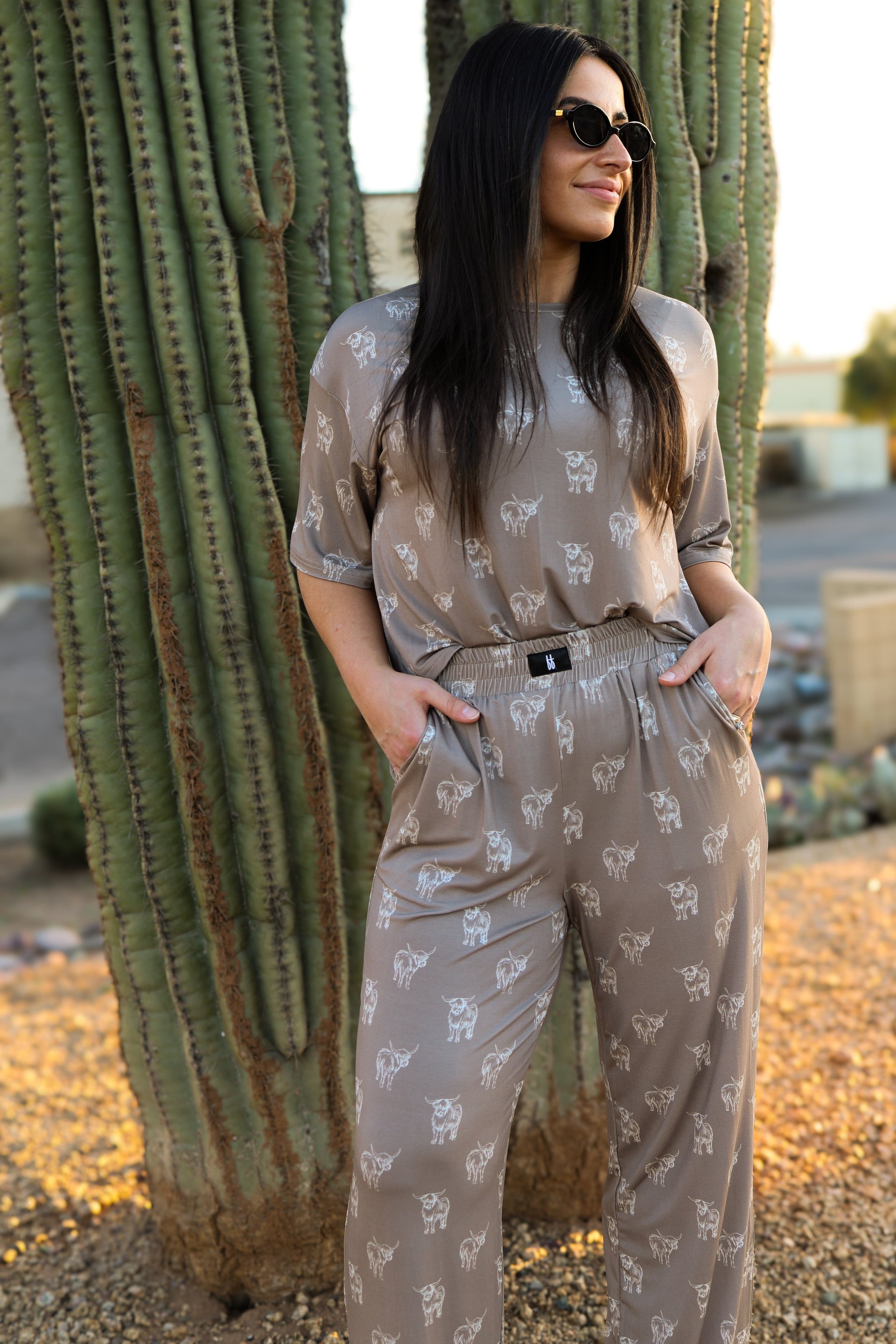 Woman wearing a taupe boxy tee and wide-leg lounge pants with a white highland cow print.
