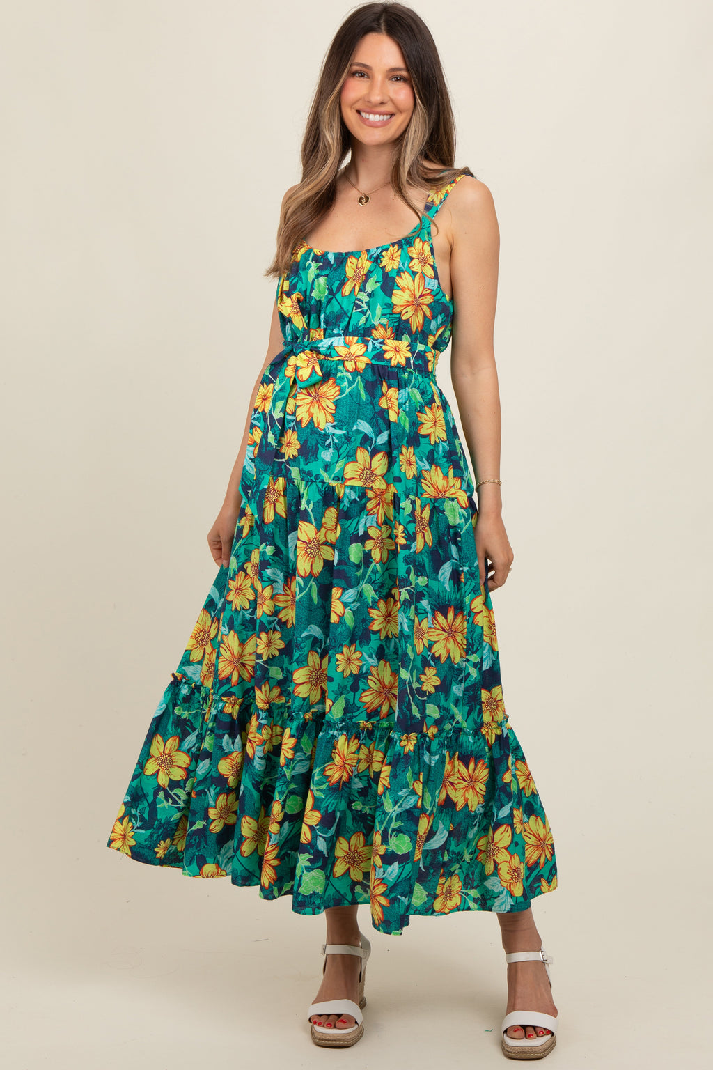 A pregnant woman smiling while wearing a yellow floral print tiered midi dress with a sash tie at the waist.