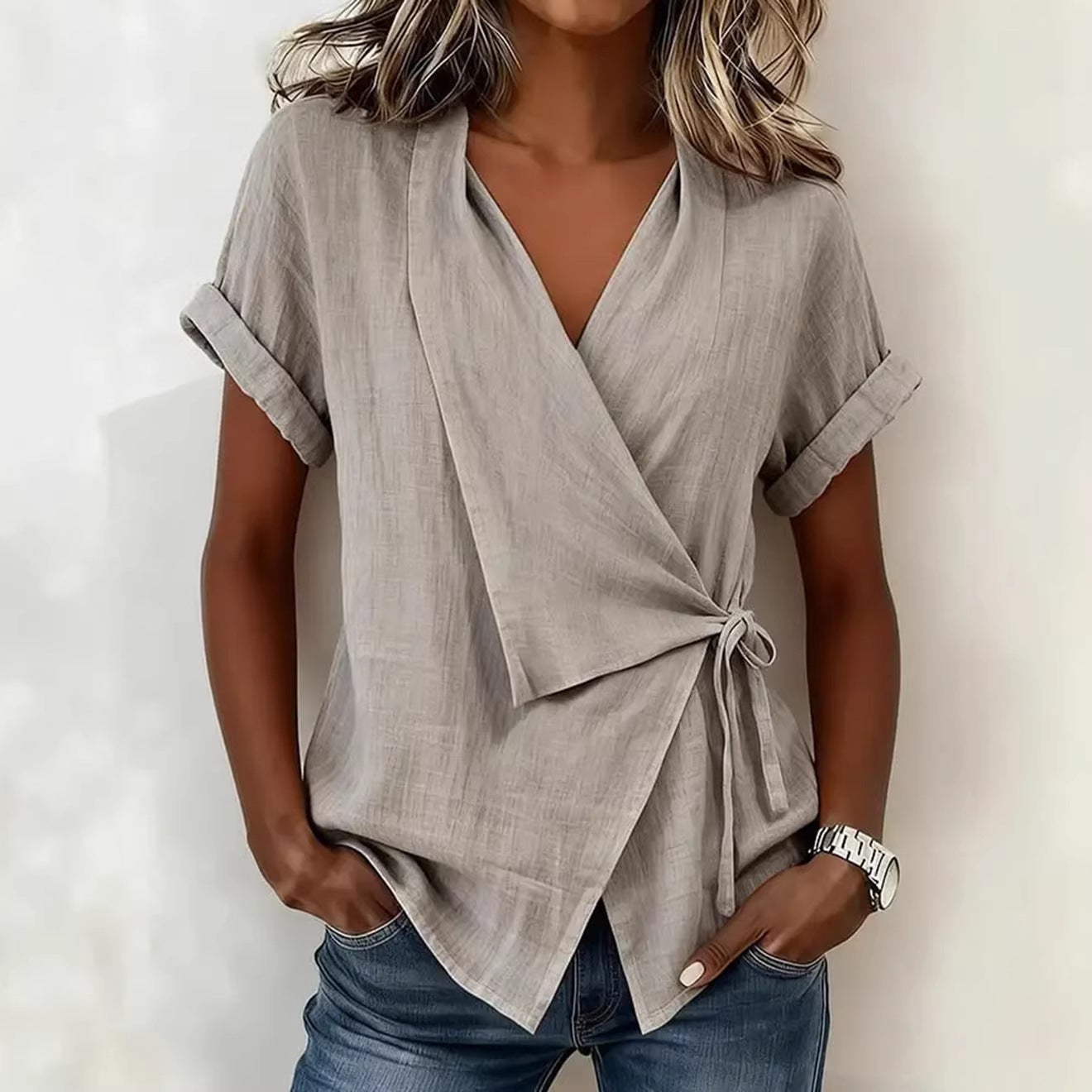 A woman wearing a casual beige or black linen-blend wrap top with a lapel collar and side lace-up tie detail.