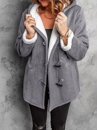 Woman wearing a hooded long-sleeve jacket with toggle closures and front pockets in solid color.