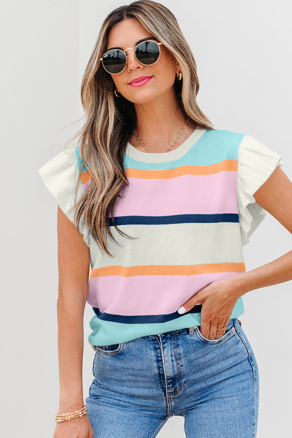 A woman wearing a Yasmin striped patchwork knit top with flutter sleeves, paired with denim jeans.