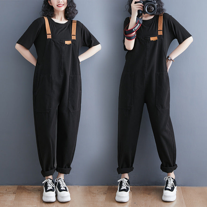 Woman wearing black Harajuku style denim overalls with tan straps and a black t-shirt, paired with white sneakers. The overalls have a relaxed fit and front patch pockets.