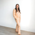 A woman wearing a peach-colored ribbed pajama set with a white rainbow pattern, featuring a button-up top and drawstring pants.